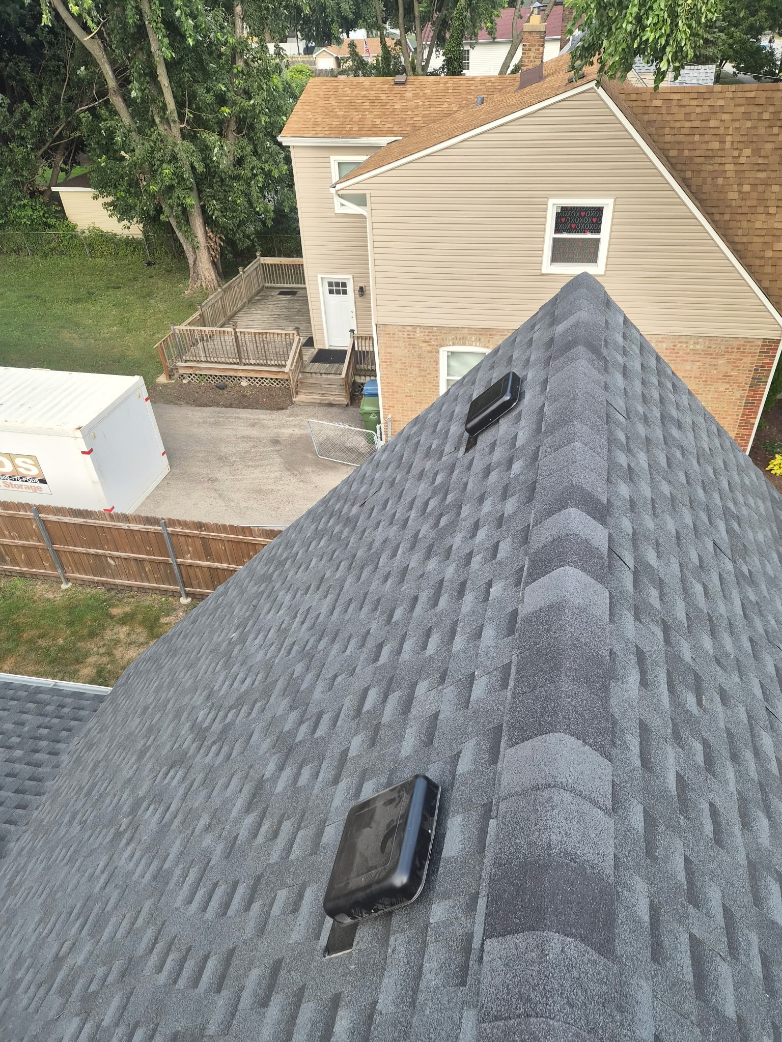 Newly installed charcoal architectural asphalt shingle roof on a Chicago-area home, showing the hip ridge line and two black roof vents